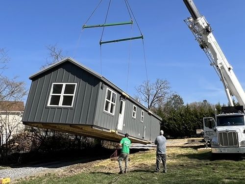 Kraan tilt een houten prefabwoning boven een tuin op