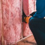 Vakman plaatst roze isolatiemateriaal tussen houten stijlen