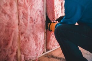 Vakman plaatst roze isolatiemateriaal tussen houten stijlen