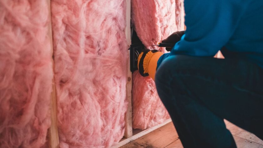 Vakman plaatst roze isolatiemateriaal tussen houten stijlen